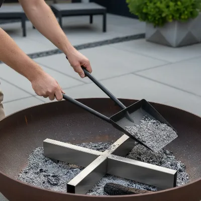 A person using a specialized shovel to remove ash from a Breeo X Series 24 fire pit, highlighting the interior design