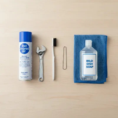 Essential tools for cleaning a clogged propane fire pit burner, including brushes, wire, and compressed air.