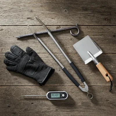 Essential tools for safe and effective fire pit cooking, including long tongs, heat-resistant gloves, and a meat thermometer.
