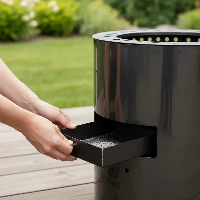 A person demonstrating how to clean a TIKI Brand fire pit by easily sliding out its ash pan, showing a clean and efficient maintenance process, in an outdoor setting.